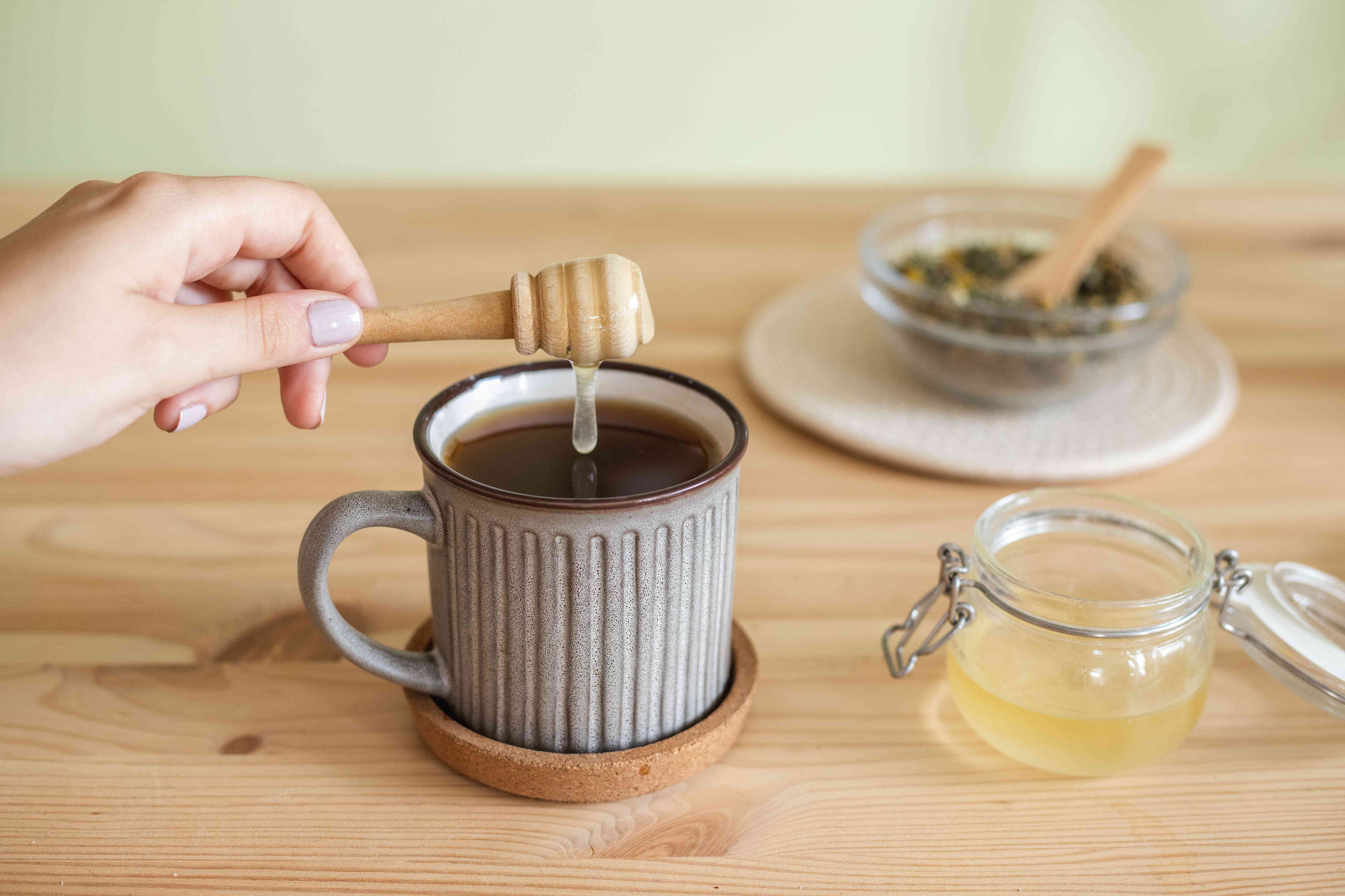 手用木制蜂蜜勺将蜂蜜滴入热茶杯中