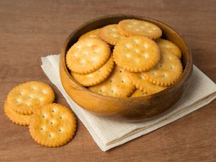 木碗中的圆形咸饼干饼干，放在亚麻和木制背景上。