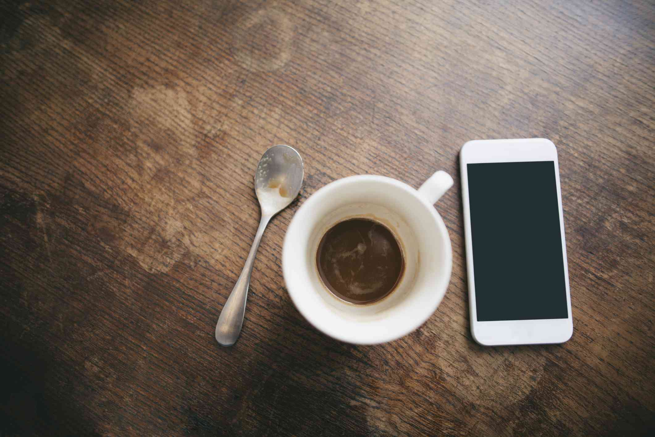 咖啡杯与剩余的咖啡，勺子和智能手机在木头上