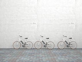 水泥墙前停着一排三辆电动自行车＂width=