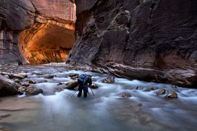 一名徒步旅行者在砂岩峡谷中走过及膝深的水＂width=