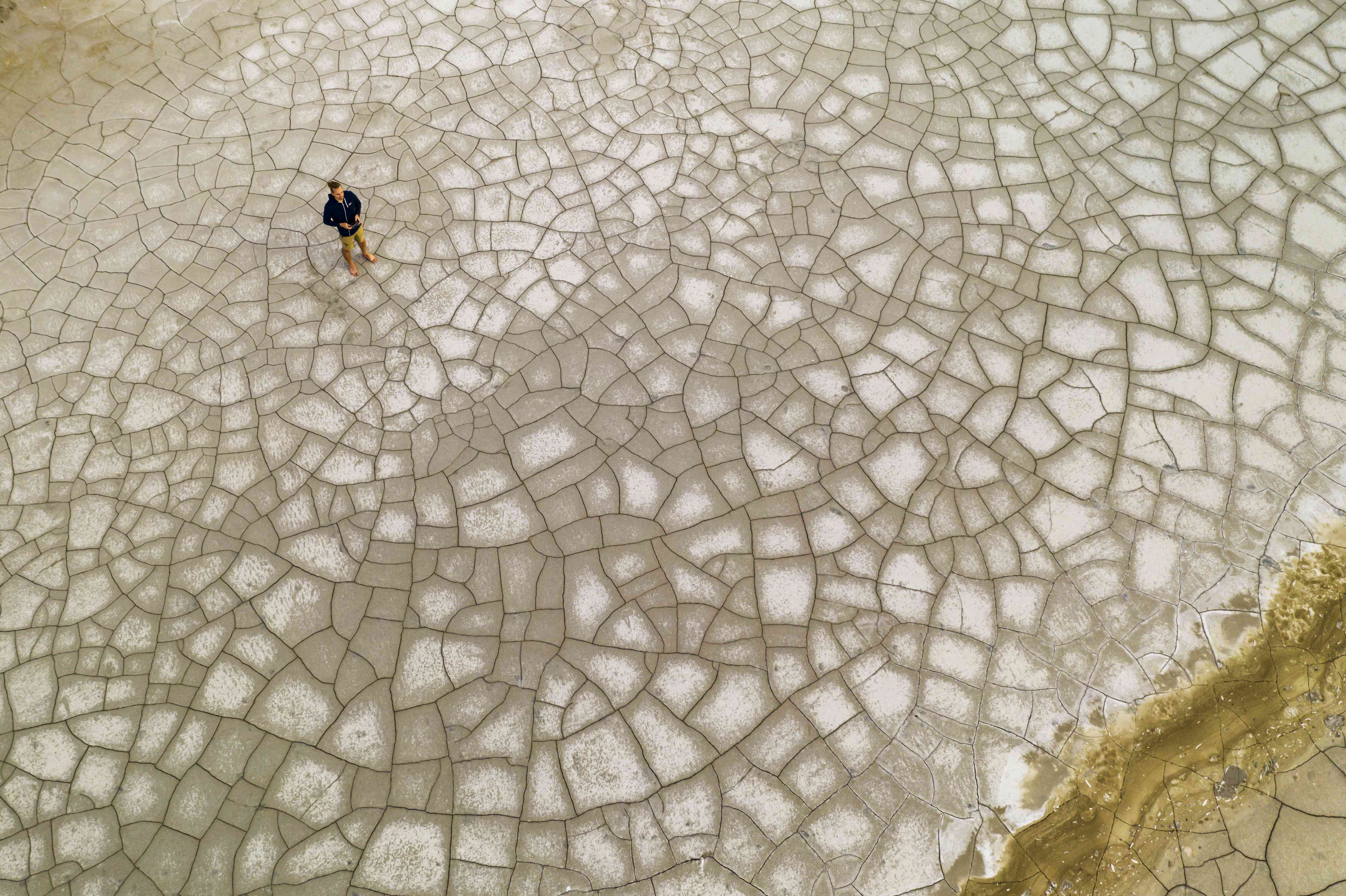 一个人站在裂缝地上的鸟瞰图。全球气候变暖的概念＂width=