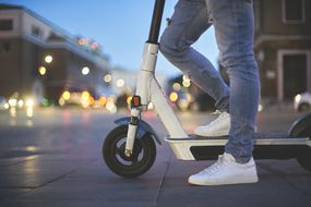 站在e-scooter＂width=