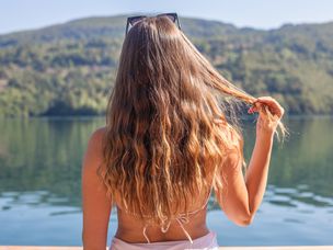 穿着泳装的女人玩着长头发，看着外面的大湖