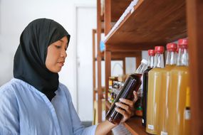 一位印尼穆斯林妇女在有机商店的货架上查看蜂蜜的标签＂width=