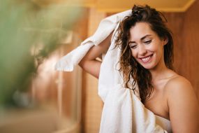 美丽快乐的女人用毛巾在浴室里擦头发。
