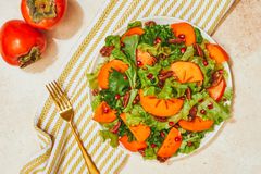 切成薄片的柿子水果和石榴种子在绿色沙拉和金叉上