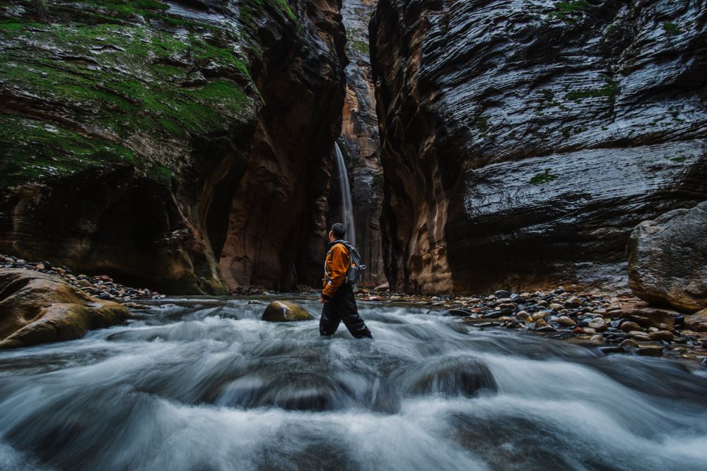 一个男人站在一条狭窄的峡谷前的小溪里
