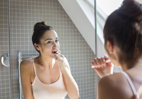 女人在浴室的镜子上刷牙。”class=