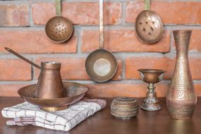shot of copper and brass cooking utensils against brick