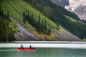 一对夫妇划着红色的独木舟在湖上划桨，以山的低坡为背景