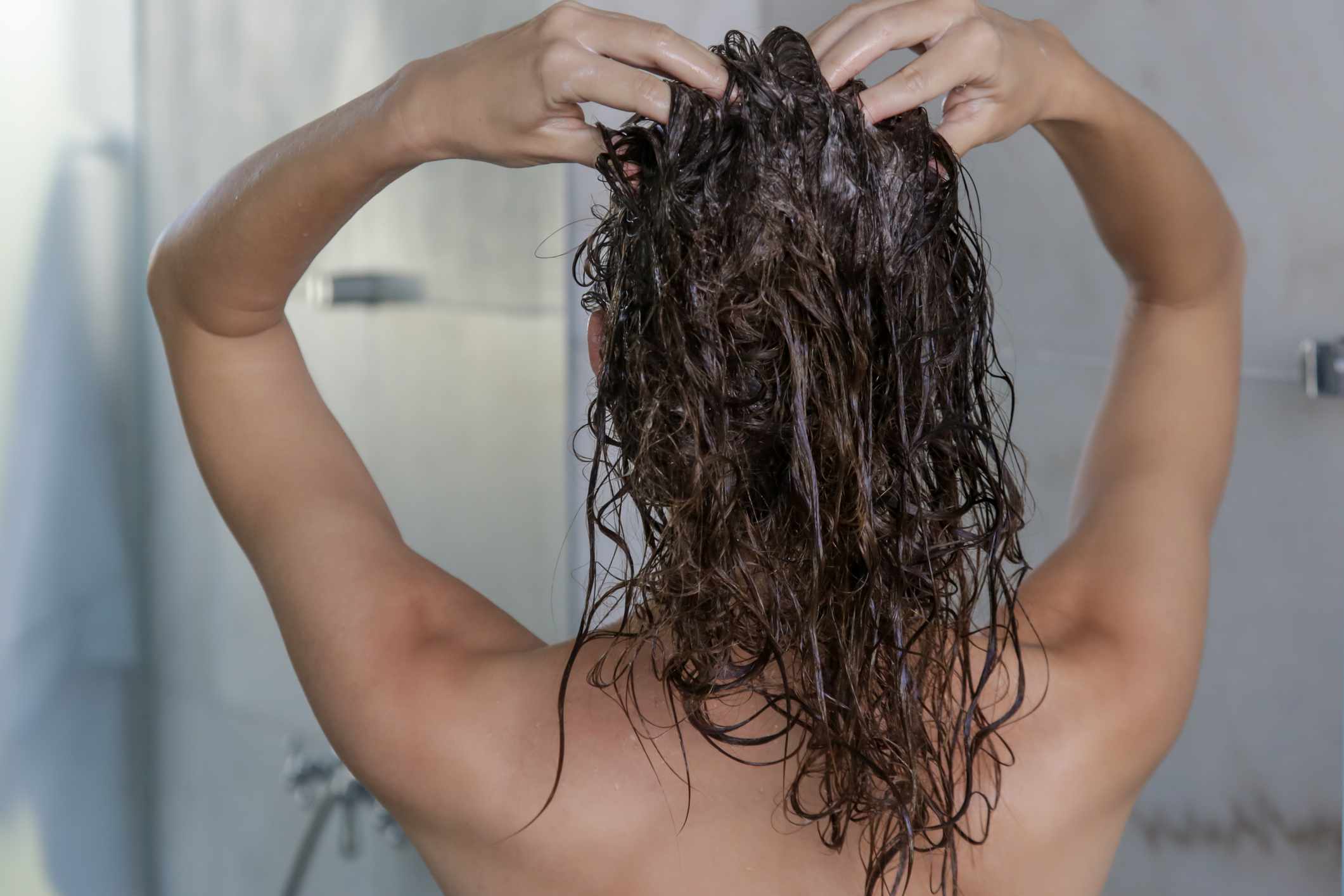 头发湿的人在淋浴时按摩头皮＂width=