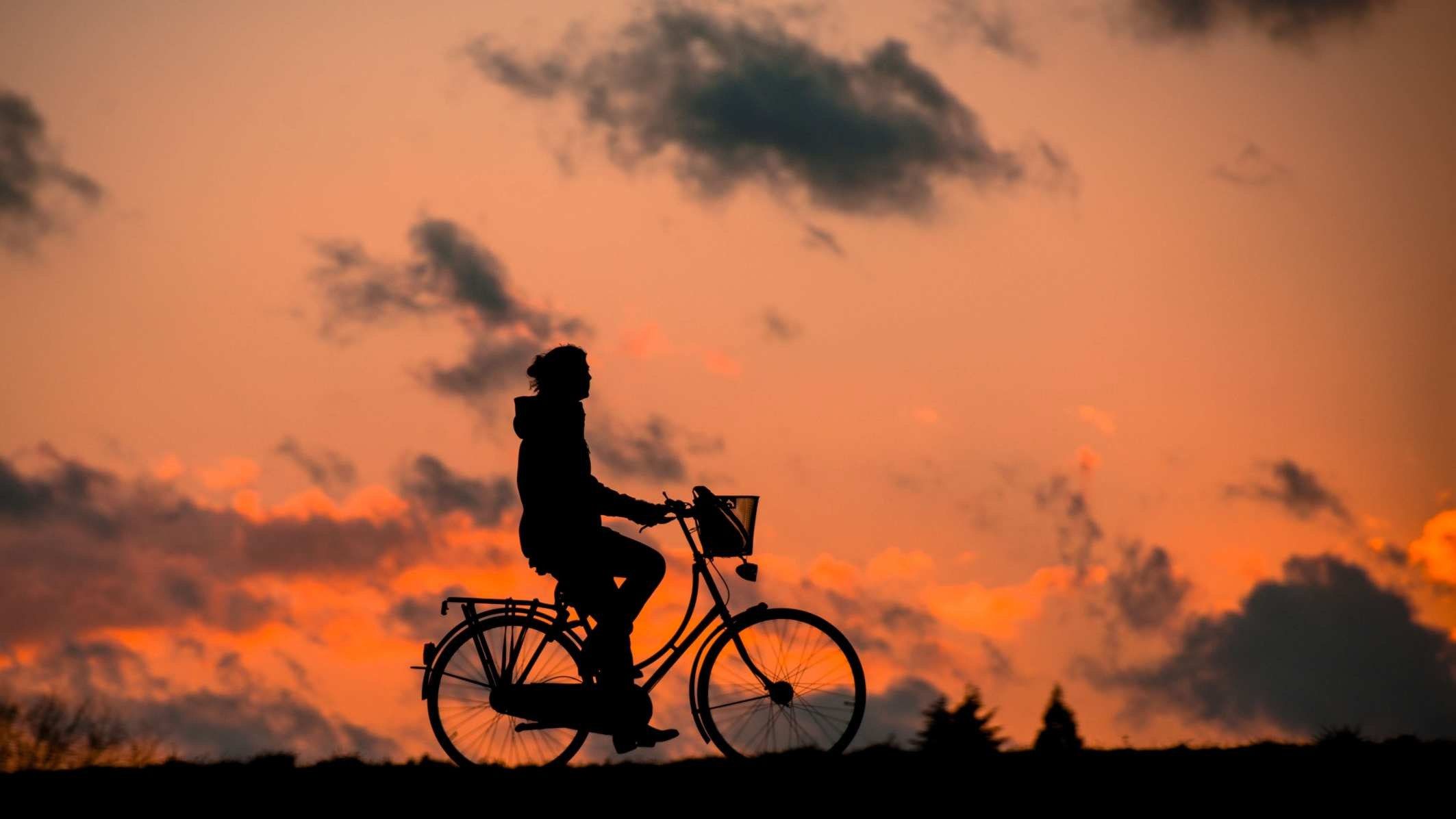 一个人骑自行车在日落的天空剪影。