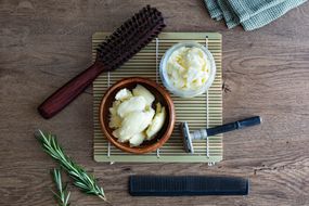 flat lay of raw shea butter in bowls with grooming and hair tools on laminate wood table