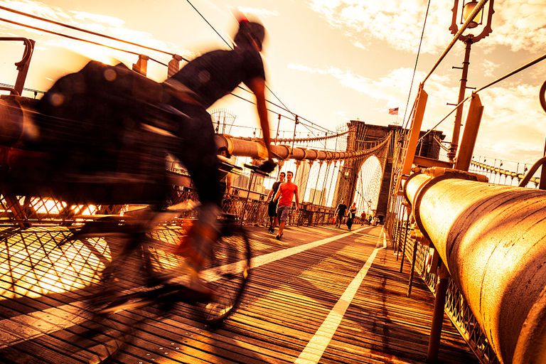 骑自行车的人骑在纽约市布鲁克林大桥上的图像。“class=