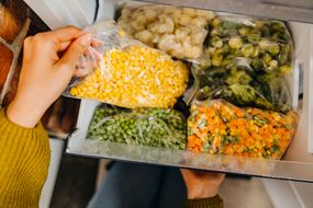 一名妇女将冷冻的蔬菜袋装进冰箱，用于膳食计划和准备
