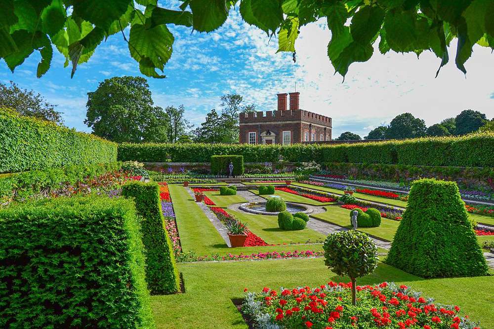 经典英语花园在蓝天下覆盖着绿色的草坪修剪得整整齐齐,塑造绿色的树篱,和床上的红色花朵在汉普顿宫面前