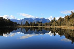 Westland Tai Poutini国家公园的山脉和森林倒映在Matheson湖上，湛蓝的天空和几朵低垂的白云