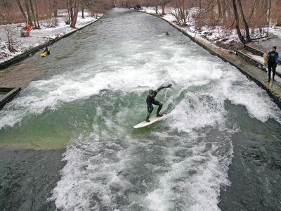 冲浪者在埃斯巴赫中部冲浪，在冬天，河两岸都是雪，还有一片棕色树叶的树林