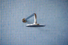 极简主义的蓝色瓷砖淋浴与现代闪亮的镀铬淋浴头“width=
