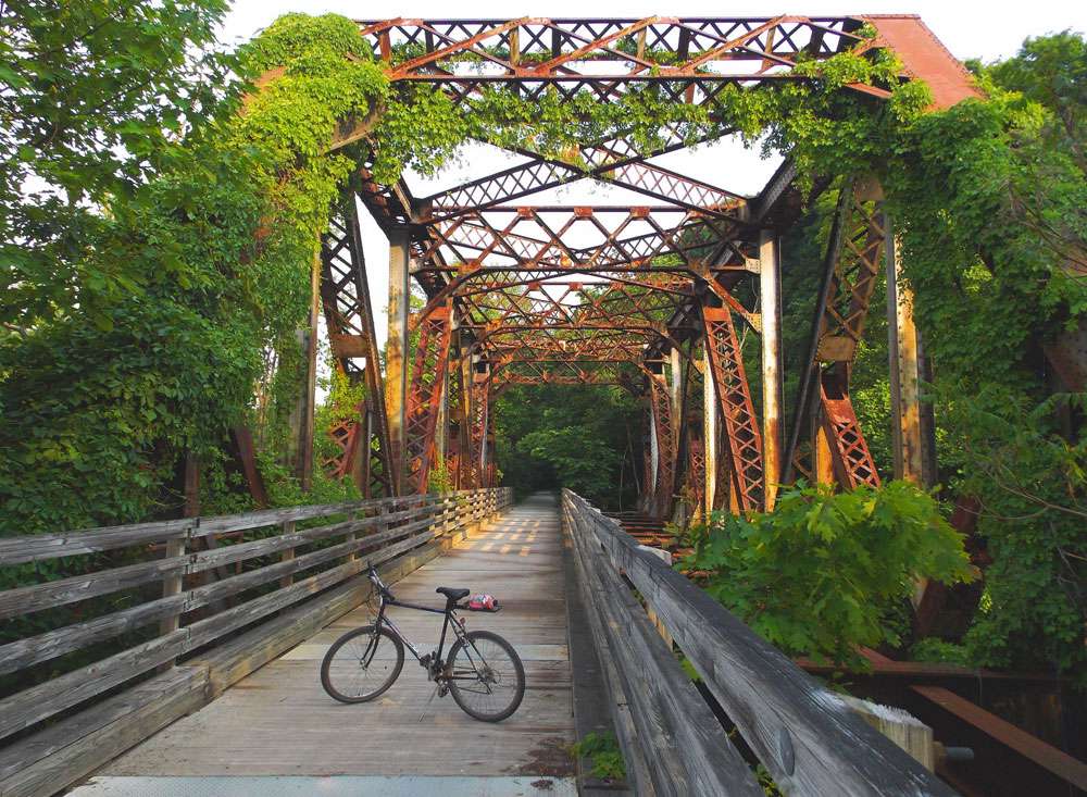 一辆自行车停在一座老铁路桥上，桥墩上爬满了常春藤