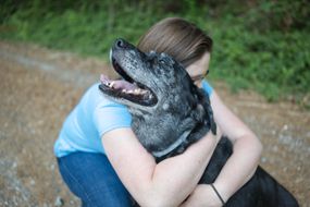 一名身穿蓝衬衫的妇女抱着一只老黑狗，它的嘴是灰色的