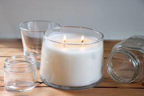 点燃了白色的蜡烛放在木桌上包围空的玻璃蜡烛罐
