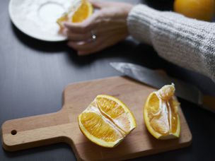 人在木制切菜板上将橙色切成两半，以便以后