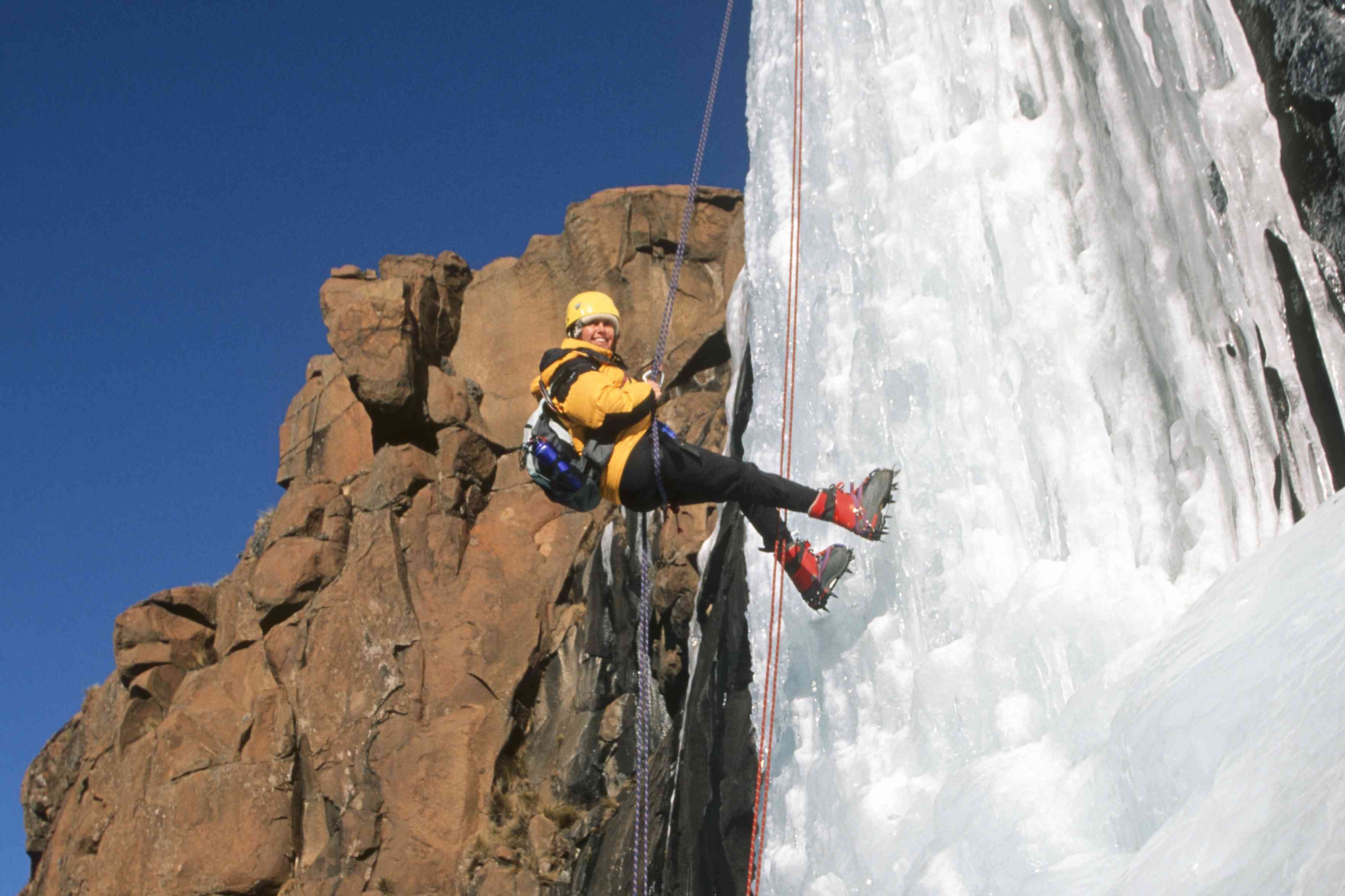 微笑的攀登者在冰冻的瀑布上，旁边是红色的岩层