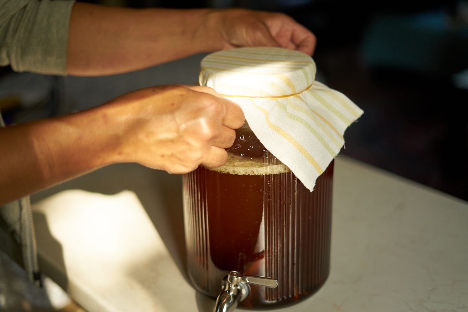 手放在大玻璃分配器上，将芝士塞盖子覆盖，用橡皮筋固定为康普茶发酵