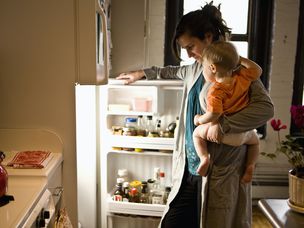 抱着儿子的母亲在冰箱里寻找食材