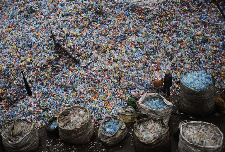 一名工人在塑料回收厂整理用过的塑料瓶＂class=
