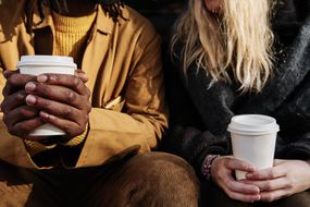 不同文化背景、互不相识的朋友坐在一起，捧着一杯咖啡。注意手部＂width=