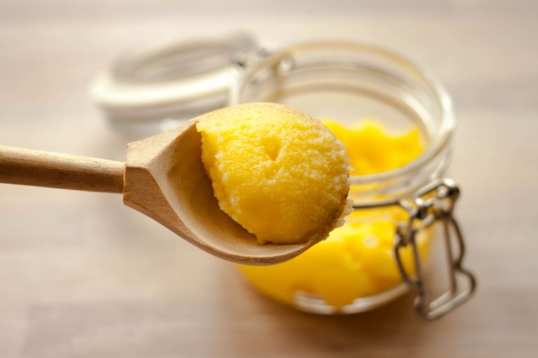 酥油在玻璃罐中澄清了黄油desi，用汤匙在天然木制背景上制成的汤匙