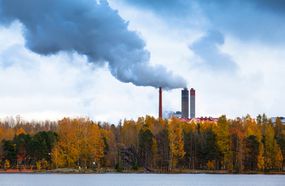 工厂排放的烟雾从湖泊和森林后面滚滚而出＂width=