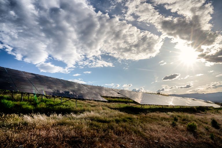 夕阳西下时，科罗拉多西部的一个太阳能农场，太阳、蓝天和云层倒映在太阳能电池板上＂class=