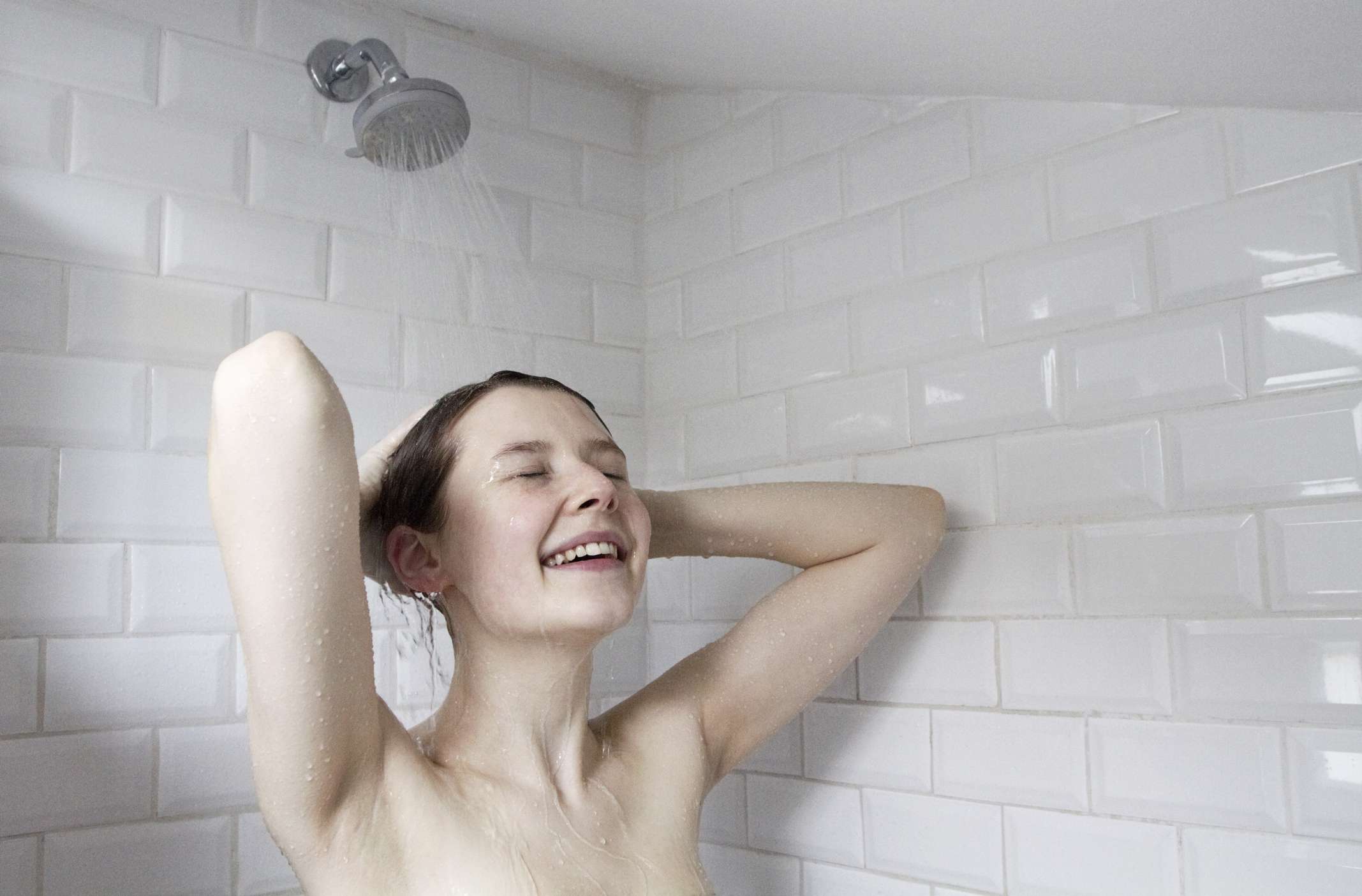 一个白人妇女在白色的地铁瓷砖淋浴间里用水洗头。