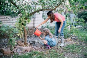 母女俩穿胶靴，在花园里给树浇水