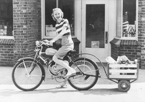 一个女人骑着一辆带货物拖车的自行车的复古照片。