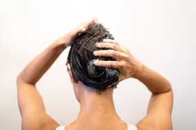 用洗发水棒洗湿头发的女人的背部＂width=