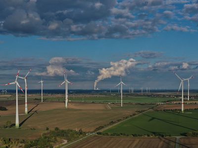 在这张鸟瞰图中，当水蒸气从德国Weissenfels附近的Kraftwerk Lippendorf燃煤发电站的冷却塔上升时，风力涡轮机在风力公园旋转。