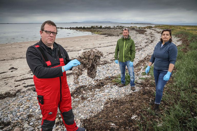 三个科学家在沙滩上扔塑料垃圾