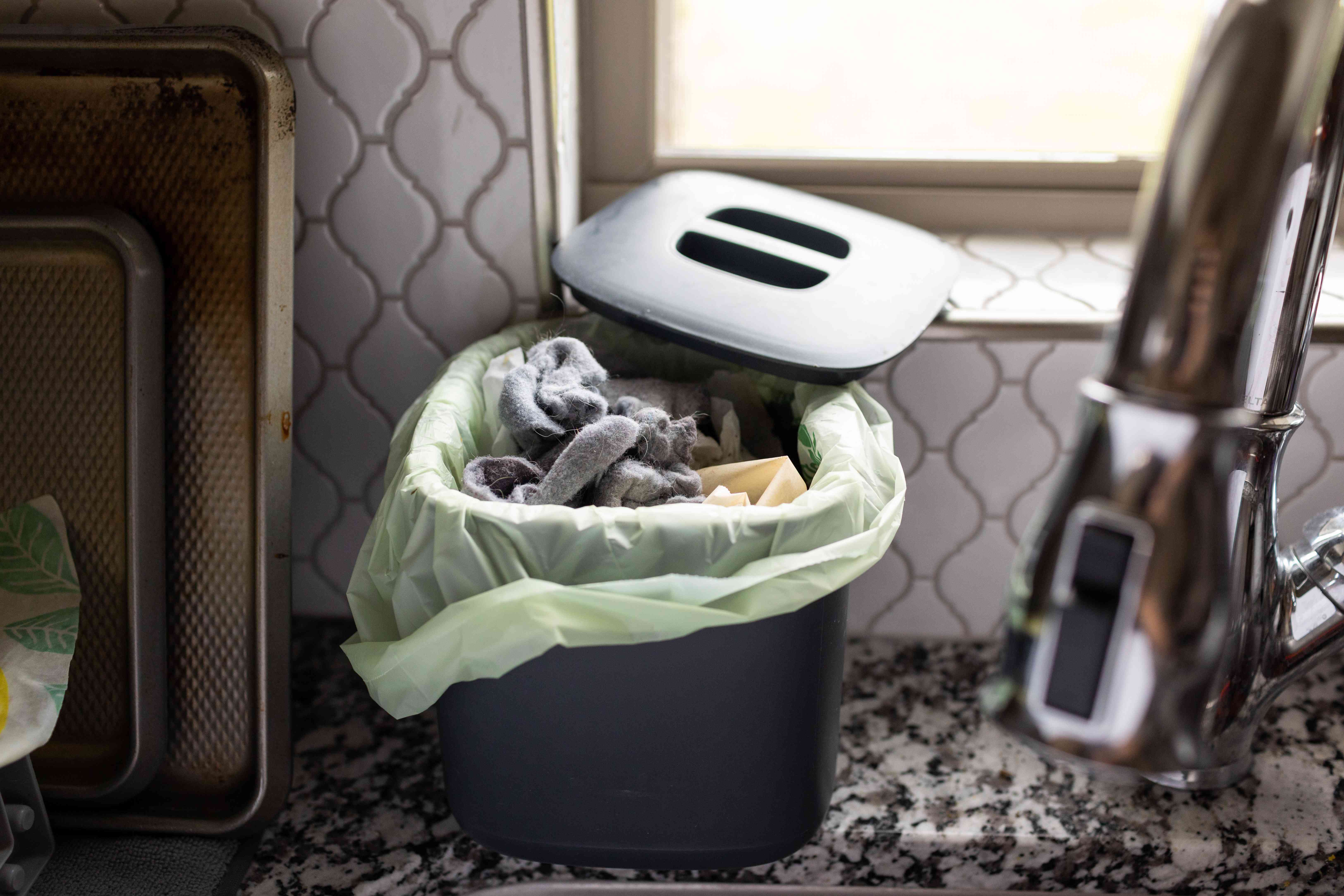 用过的灰色干衣机棉塞在水槽旁边的厨房堆肥箱里＂width=