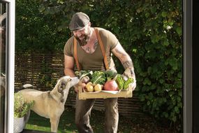 一名纹身男子给狗狗看一盒新鲜蔬菜。