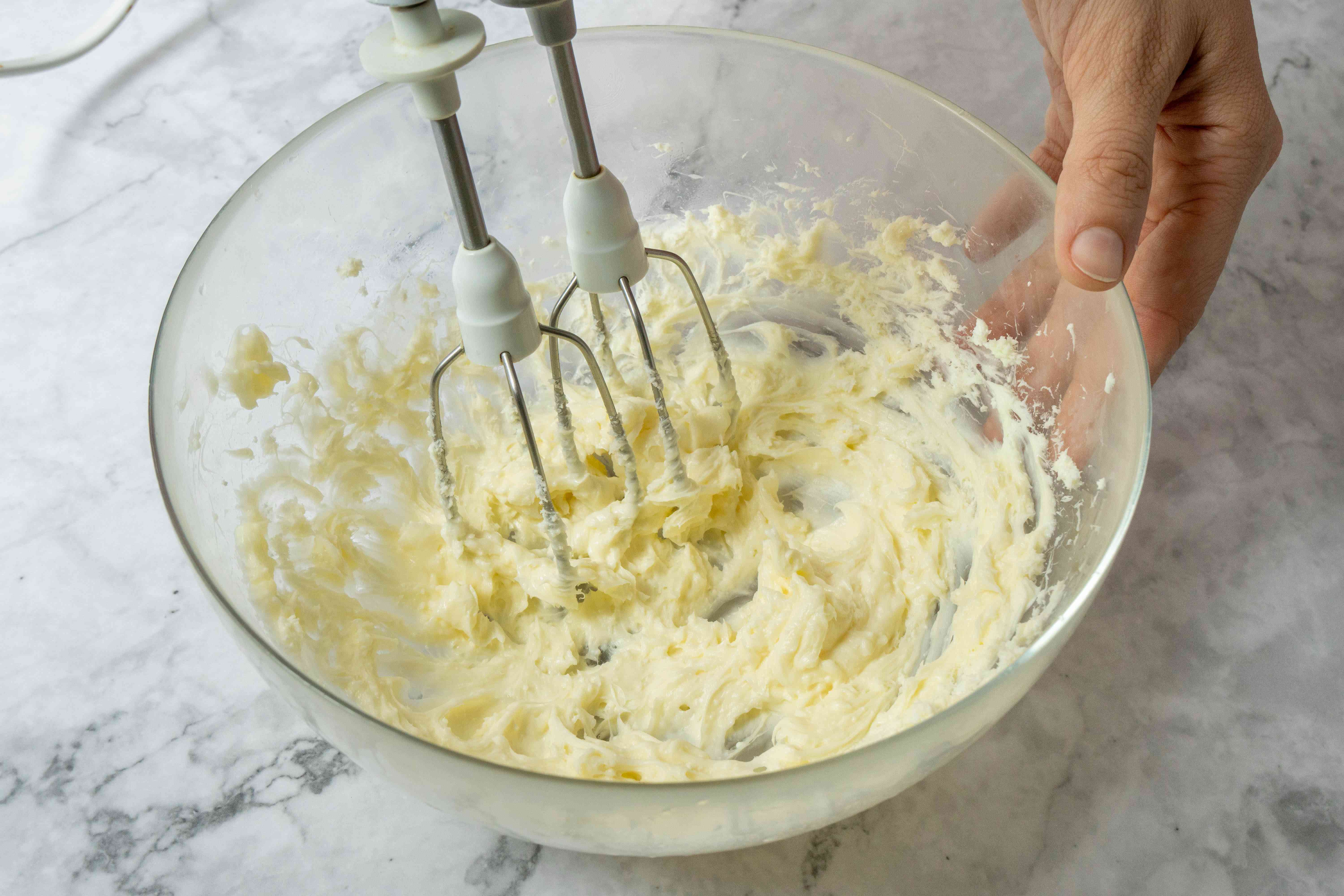 白色的手工搅拌器将融化的乳木果油和油在玻璃碗中搅拌成奶油状的混合物