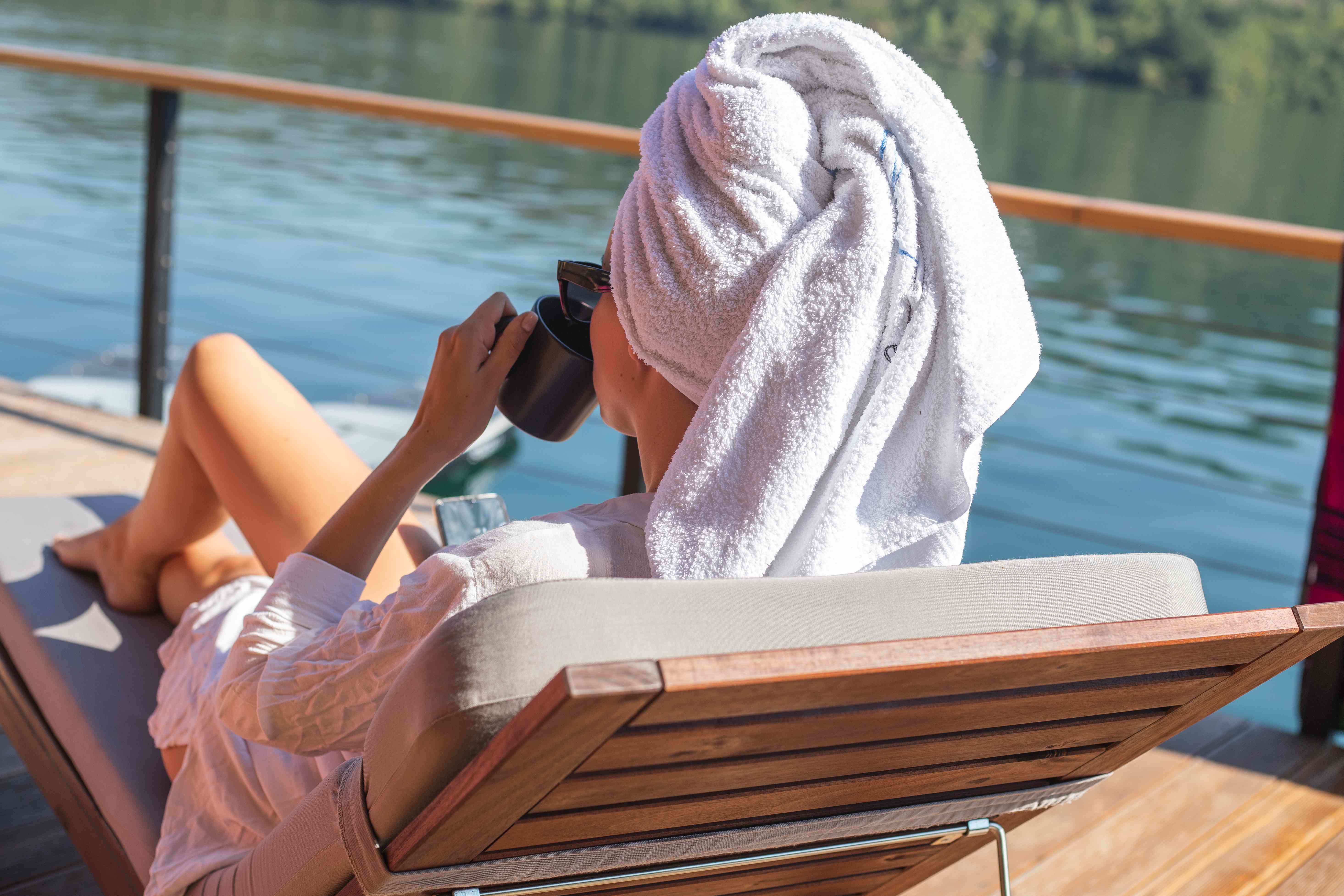 女人在湖上的躺椅上放松身心，而头发被包裹在毛巾上以进行深层调理