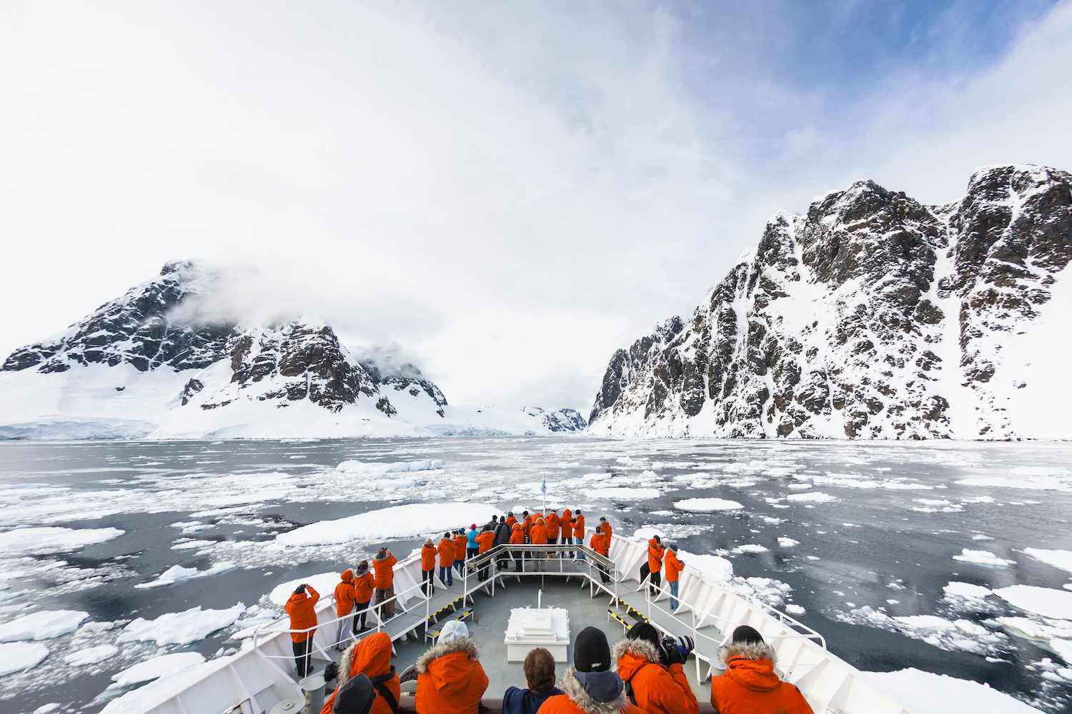 一艘载着身穿橙色外套的乘客的游轮抵达南极洲岩石和结冰的海岸