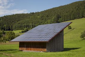 在开阔的田野里，太阳能电池板覆盖着一个棚子。