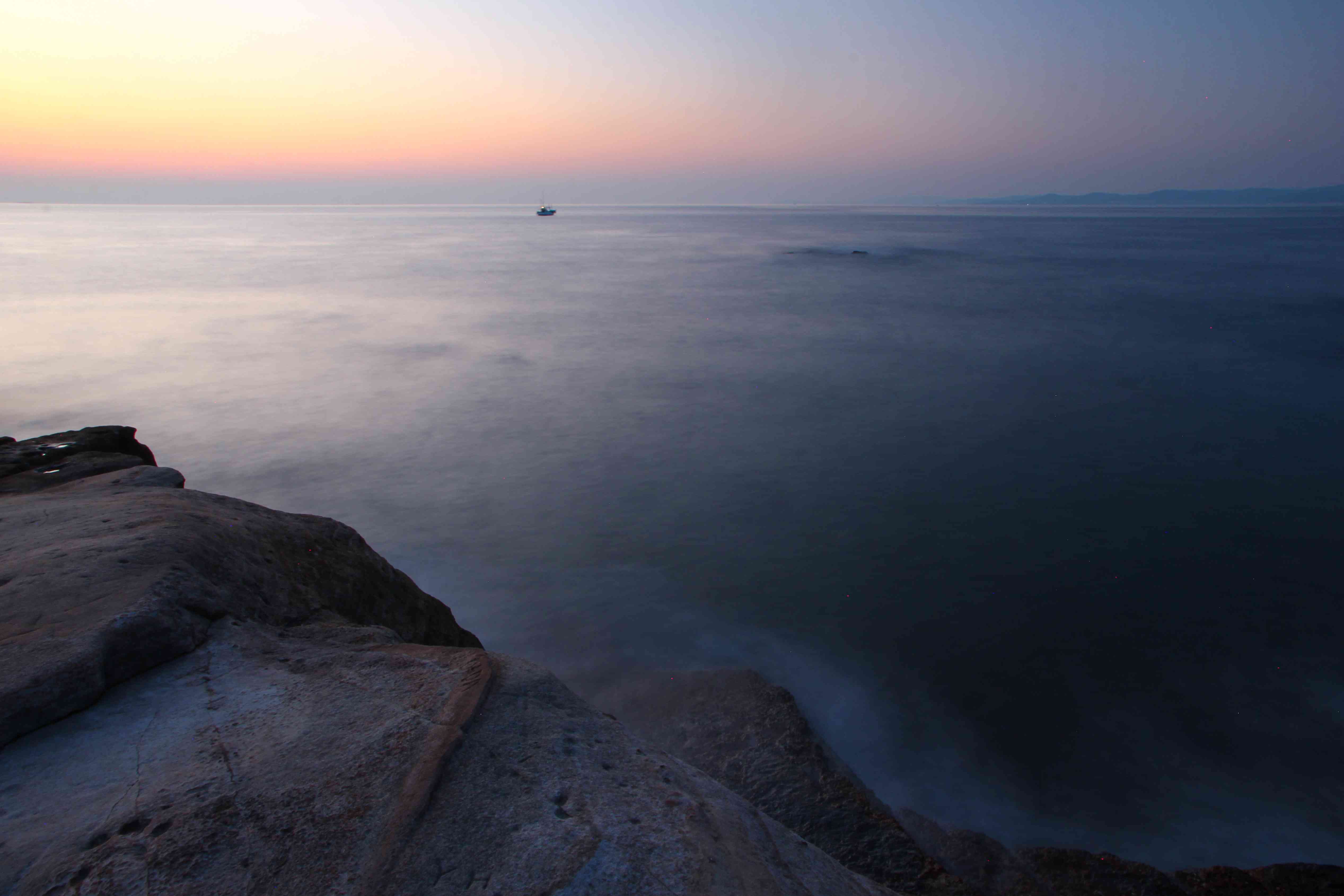日出时沿海岸的海洋与雾和小船在地平线上的恐怖镜头