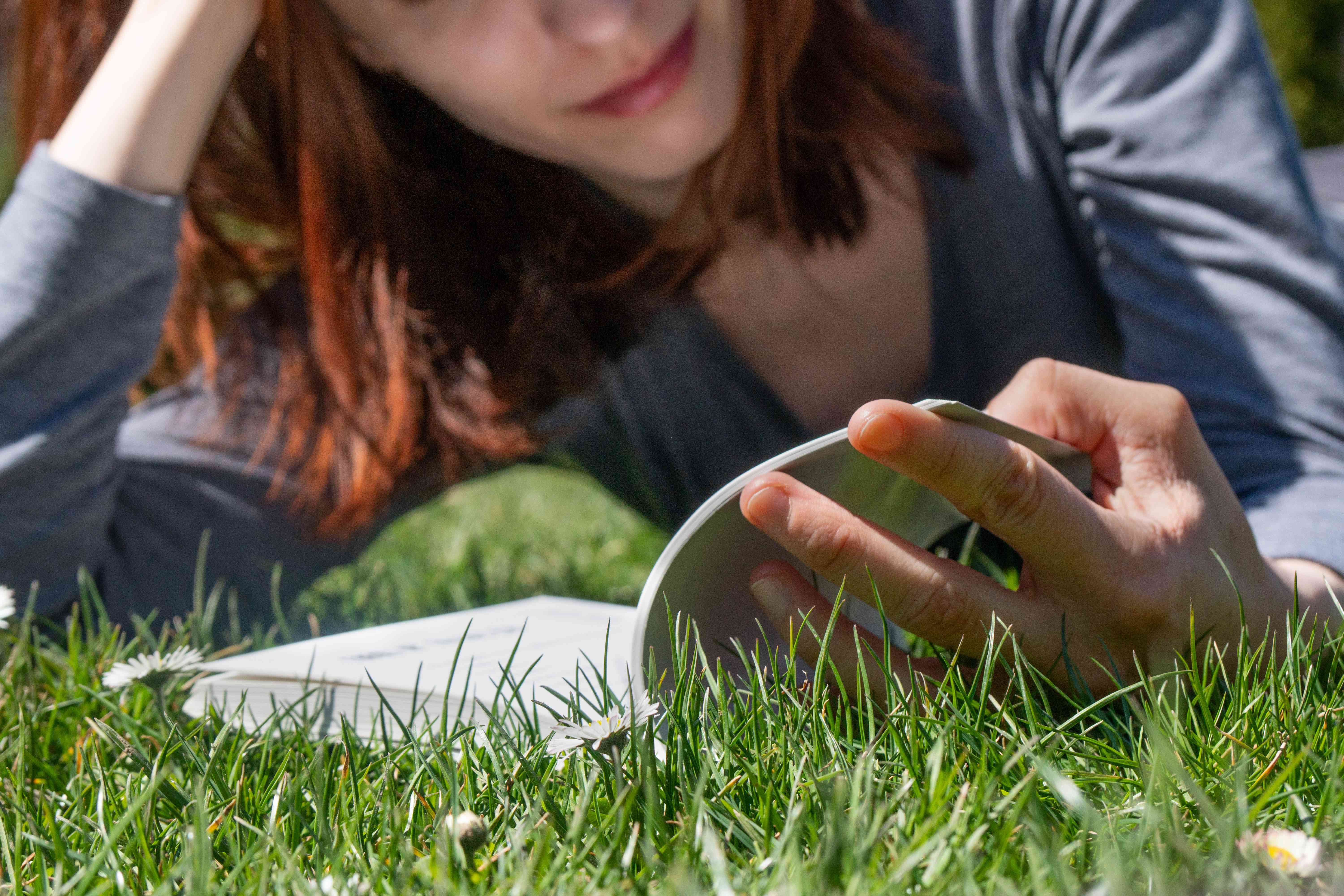 在一个阳光明媚的日子里，女人躺在绿色的草地上看书
